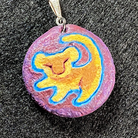 A tiny pendant with a stylized Simba engraved in it, inspired by the Sega Genesis checkpoint from The Lion King game.